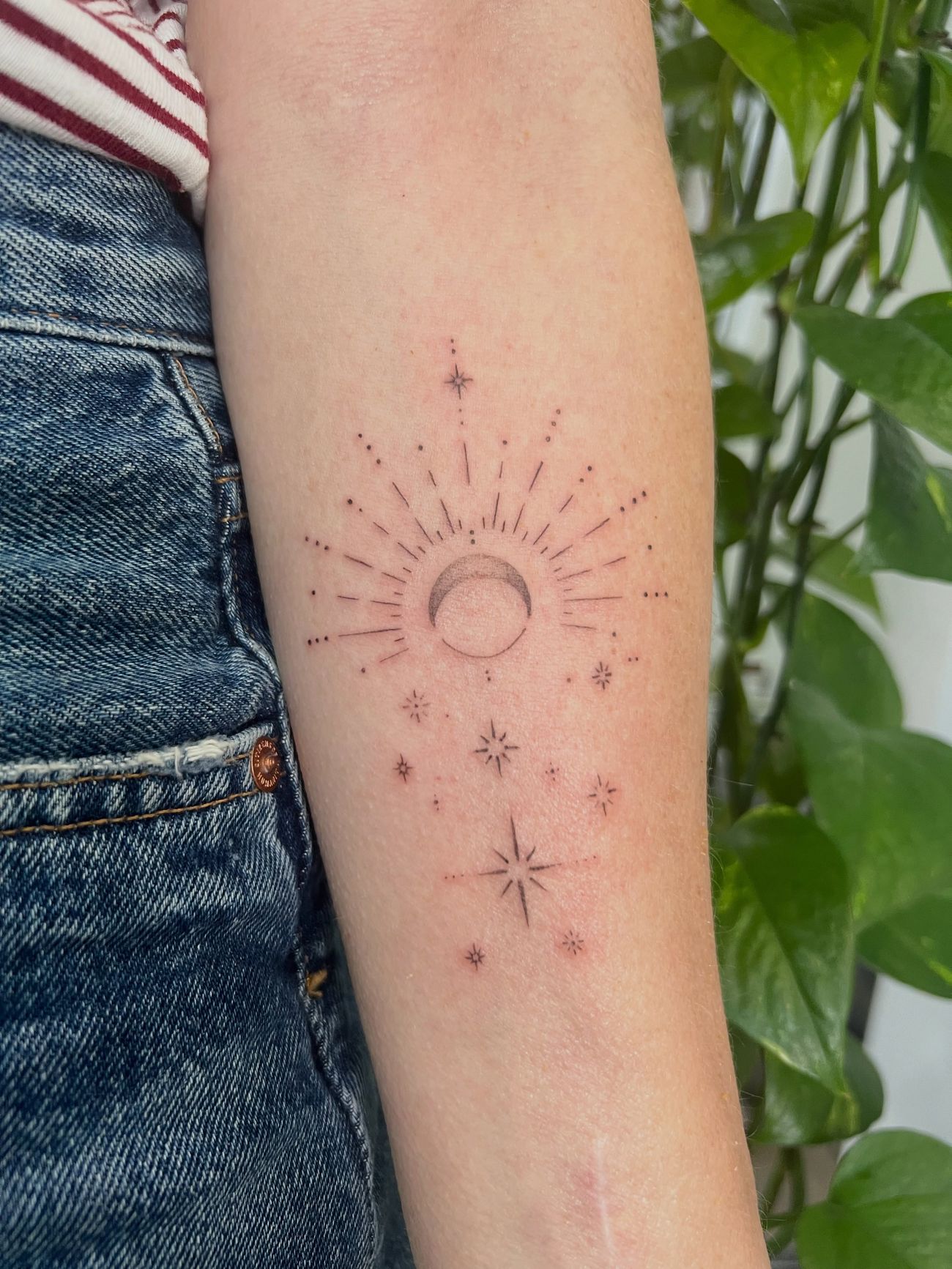 A fine line crescent moon radiating thin lines and small stars on an upper arm