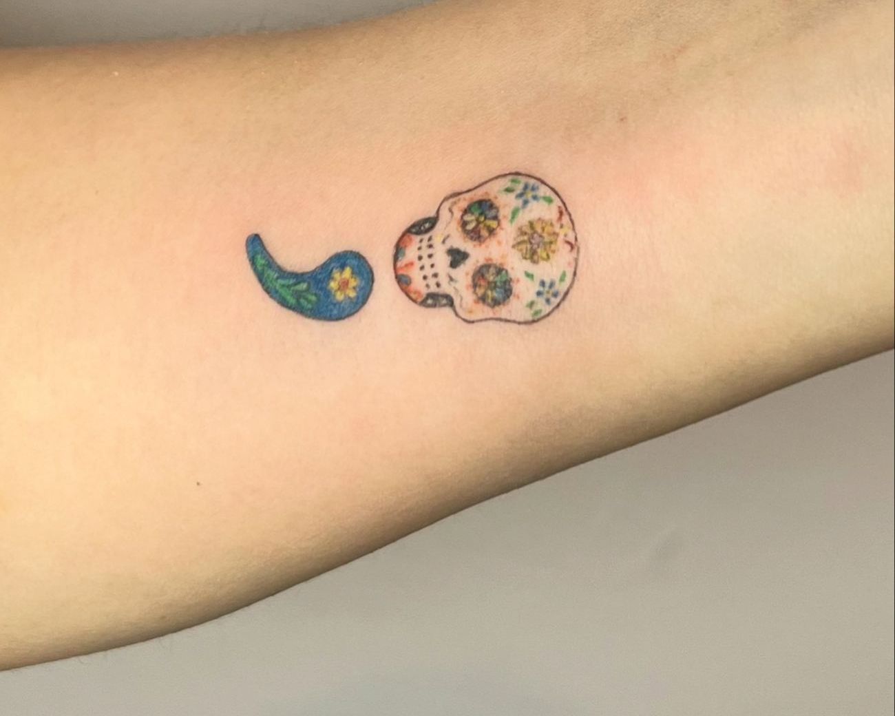A tiny sugar skull and a blue botanical semicolon on the inner wrist